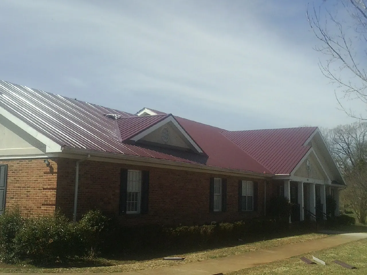 Red metal roof with gabled entries on a long brick building, from a Hail Damage Roof Repair job in Shawmut