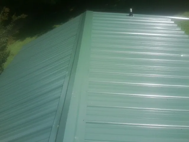 New green metal panels meeting at the ridge of a roof — Flat Roof Repair work by our crew in Shawmut